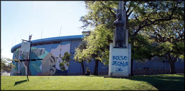 Ao fundo o Estádio Centenário. Estátua com pichação de protesto.